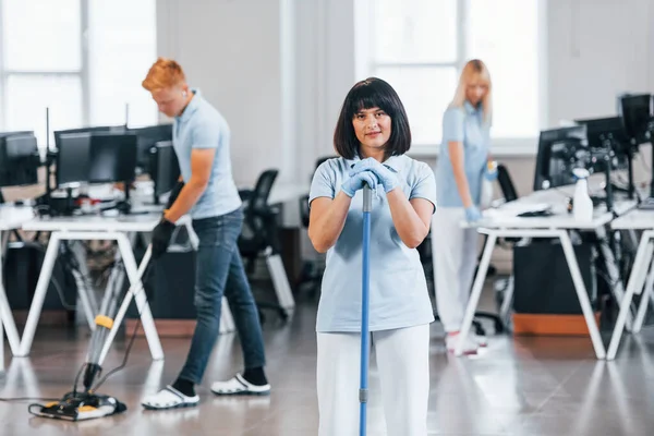 Cleans floor. Group of workers clean modern office together at daytime.