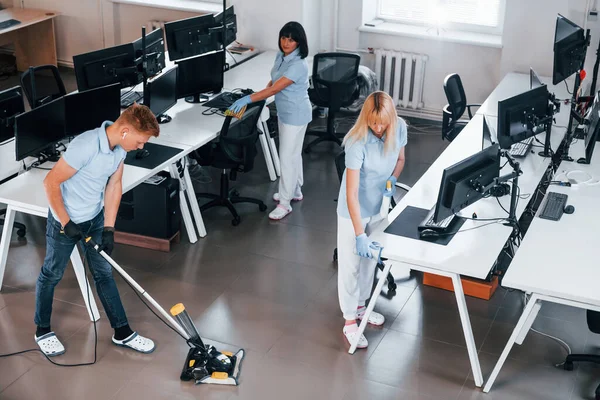 Cleans floor. Group of workers clean modern office together at daytime.