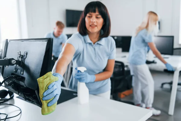 Cleans monitor. Group of workers clean modern office together at daytime.