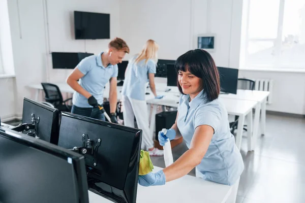 Cleans monitor. Group of workers clean modern office together at daytime.