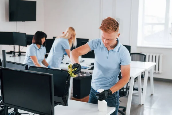 Cleans monitor. Group of workers clean modern office together at daytime.