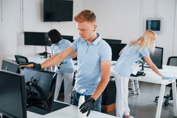 Cleans monitor. Group of workers clean modern office together at daytime.