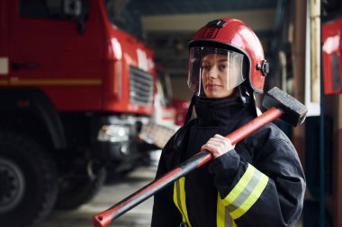 Ellerinde çekiçle. Koruyucu üniformalı kadın itfaiyeci kamyonun yanında duruyor..