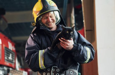 Koruyucu üniformalı itfaiyecinin portresi. İçinde küçük sevimli siyah bir kedi var..