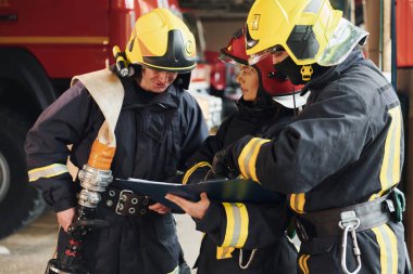 With notepad. Group of firefighters in protective uniform that is on station.
