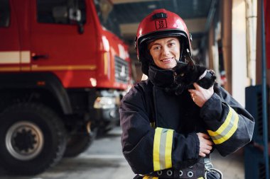 Şirin siyah kedi. Koruyucu üniformalı kadın itfaiyeci kamyonun yanında duruyor..
