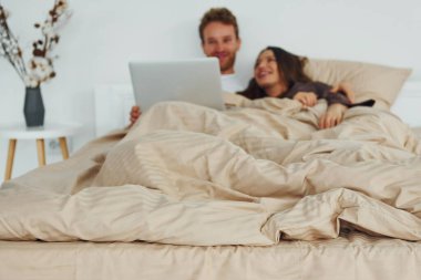 Çift dizüstü bilgisayarla yatakta yatıyor. Gündüz vakti güzel, modern yatak odasının iç tasarımı ve tasarımı..