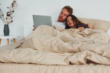 Çift dizüstü bilgisayarla yatakta yatıyor. Gündüz vakti güzel, modern yatak odasının iç tasarımı ve tasarımı..