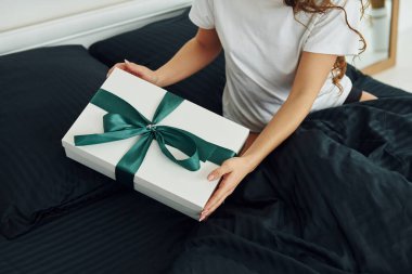 Hediye kutusu genç bir kadının elinde. Gündüz vakti güzel, modern yatak odasının iç tasarımı ve tasarımı..