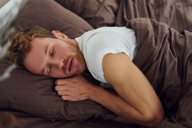 Man sleeps on the bed. Interior and design of beautiful modern bedroom at daytime.