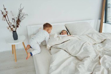 Two kids have fun while liyng down on bed. Interior and design of beautiful modern bedroom at daytime.