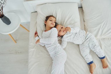 Two kids have fun while liyng down on bed. Interior and design of beautiful modern bedroom at daytime.
