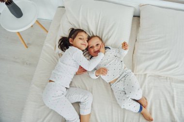 İki çocuk yatağa uzanırken eğleniyor. Gündüz vakti güzel, modern yatak odasının iç tasarımı ve tasarımı..