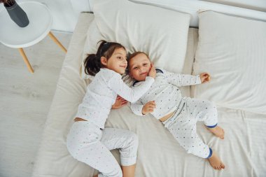 Two kids have fun while liyng down on bed. Interior and design of beautiful modern bedroom at daytime.