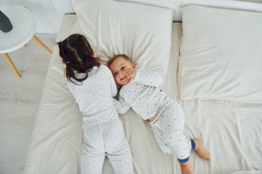 Two kids have fun while liyng down on bed. Interior and design of beautiful modern bedroom at daytime.