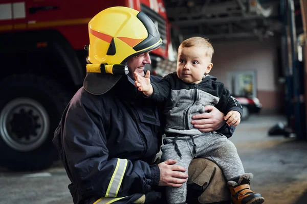 Cute little boy is with male firefighter in protective uniform.