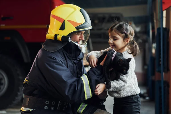 可爱的黑猫 快乐的小女孩和身穿防护服的男性消防员在一起 — 图库照片