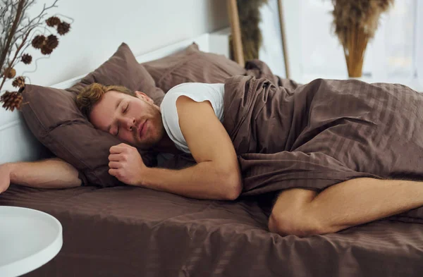 Adam yatakta uyuyor. Gündüz vakti güzel, modern yatak odasının iç tasarımı ve tasarımı..