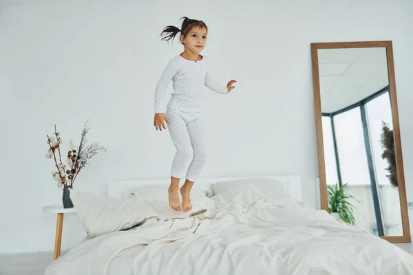 Active little girl jumps on the bed. Interior and design of beautiful modern bedroom at daytime.