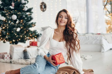 Mutlu genç kadın Noel ağacının yanında oturuyor ve yeni yılı kutluyor..