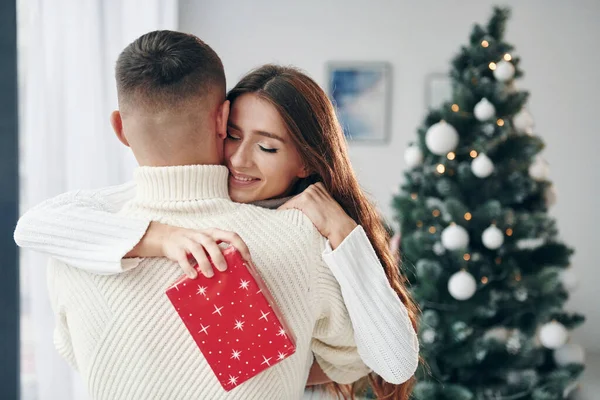 女の子は赤いギフトボックスを持っています 若いロマンチックなカップルは屋内で一緒に新年を祝う — ストック写真