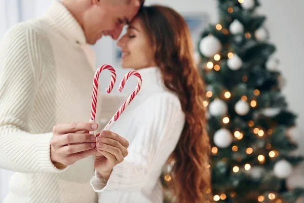 手に飴を持っている 若いロマンチックなカップルは屋内で一緒に新年を祝う — ストック写真