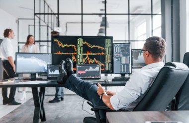 Adam sandalyeye oturur ve mola verir. Borsacılardan oluşan bir ekip modern ofiste birçok ekran ekranı ile çalışır..