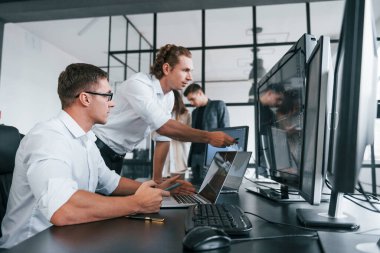 Gözlüklü adam işine odaklanmış. Borsacılardan oluşan ekip birçok ekranla modern ofiste..