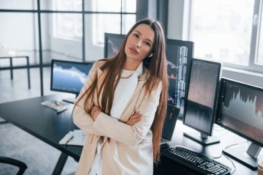 Kameraya poz ver. Genç bayan borsacı ofisin içinde. Ekranların çoğu.