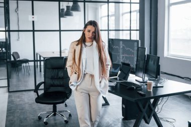 Kameraya poz ver. Genç bayan borsacı ofisin içinde. Ekranların çoğu.