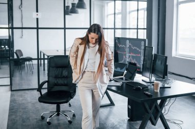 Kameraya poz ver. Genç bayan borsacı ofisin içinde. Ekranların çoğu.