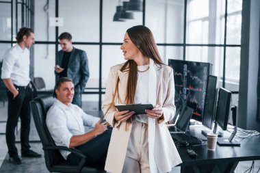 Resmi olarak genç bir kadın insanların önünde giyinir. Borsacılardan oluşan bir ekip modern ofiste birçok ekran ekranı ile çalışır..