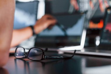 Gözlüklerin, not defterinin, belgelerin ve arka plandaki adamın odaklanmış görünümünü kapat.