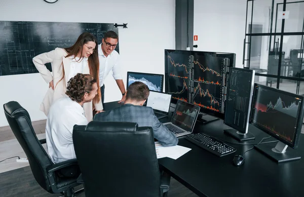 Attention to details. Team of stockbrokers works in modern office with many display screens.