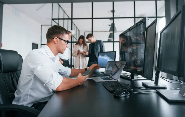 Guy in glasses concentrated at work. Team of stockbrokers is in modern office with many display screens.