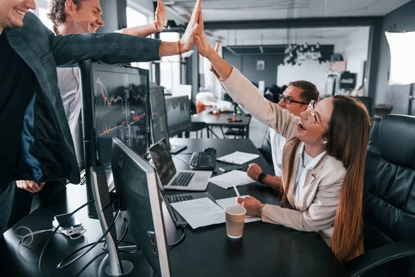 Giving high five. Team of stockbrokers works in modern office with many display screens.