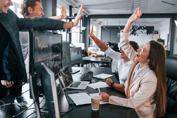 Giving high five. Team of stockbrokers works in modern office with many display screens.