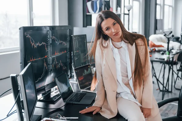 Kameraya poz ver. Genç bayan borsacı ofisin içinde. Ekranların çoğu.