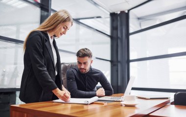 Resmi giyinmiş bir kadın ve bir adam ofis içinde masa başında birlikte çalışıyorlar..