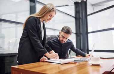 Resmi giyinmiş bir kadın ve bir adam ofis içinde masa başında birlikte çalışıyorlar..