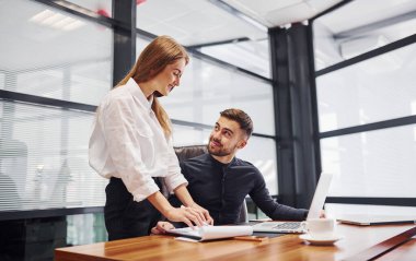 Resmi giyinmiş bir kadın ve bir adam ofis içinde masa başında birlikte çalışıyorlar..