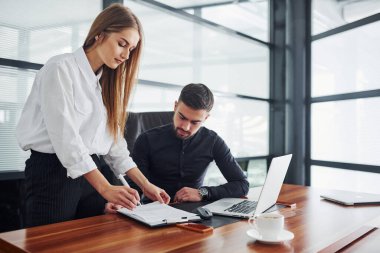 Resmi giyinmiş bir kadın ve bir adam ofis içinde masa başında birlikte çalışıyorlar..