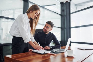 Resmi giyinmiş bir kadın ve bir adam ofis içinde masa başında birlikte çalışıyorlar..