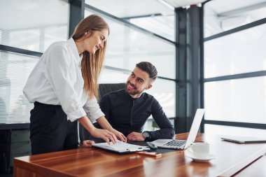 Resmi giyinmiş bir kadın ve bir adam ofis içinde masa başında birlikte çalışıyorlar..