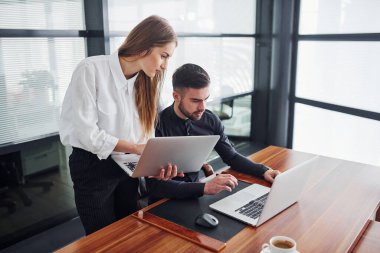 Resmi giyinmiş bir kadın ve bir adam ofis içinde masa başında birlikte çalışıyorlar..