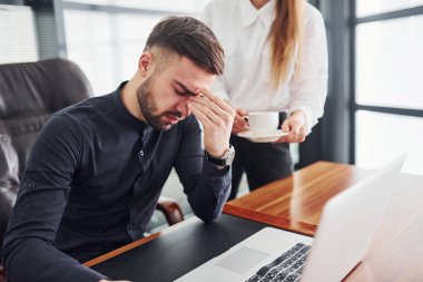 Adam kendini kötü hissediyor. Resmi giyinmiş bir kadın ve bir adam ofis içinde masa başında birlikte çalışıyorlar..