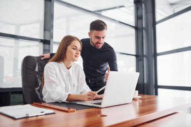 Resmi giyinmiş bir kadın ve bir adam ofis içinde masa başında birlikte çalışıyorlar..