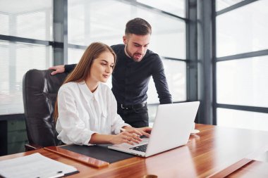 Resmi giyinmiş bir kadın ve bir adam ofis içinde masa başında birlikte çalışıyorlar..