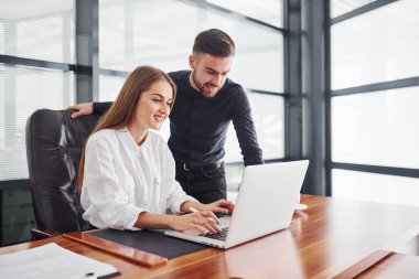 Resmi giyinmiş bir kadın ve bir adam ofis içinde masa başında birlikte çalışıyorlar..