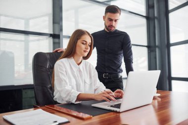 Resmi giyinmiş bir kadın ve bir adam ofis içinde masa başında birlikte çalışıyorlar..
